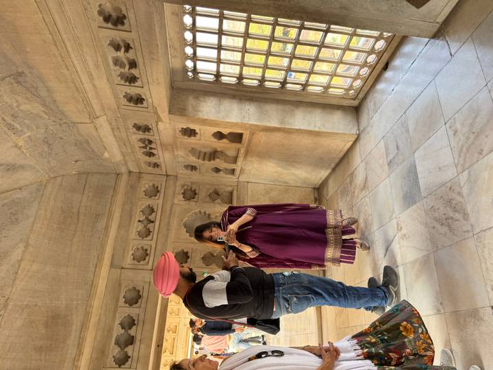 Man shows phone to woman dressed in traditional attire inside ornate marble chamber.