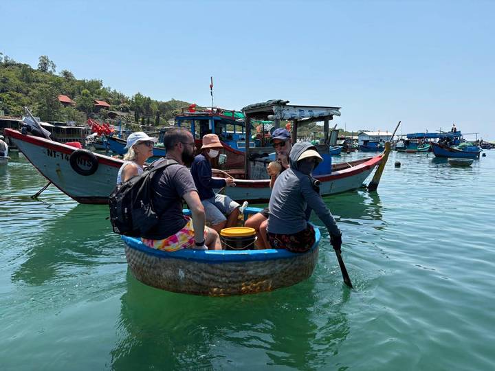 Travelers sit in a traditional round basket boat on turquoise water surrounded by colorful fishing boats.