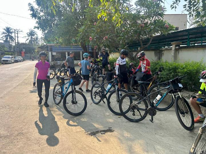 Cycling group gathered with bikes on a shaded village street before starting their ride.