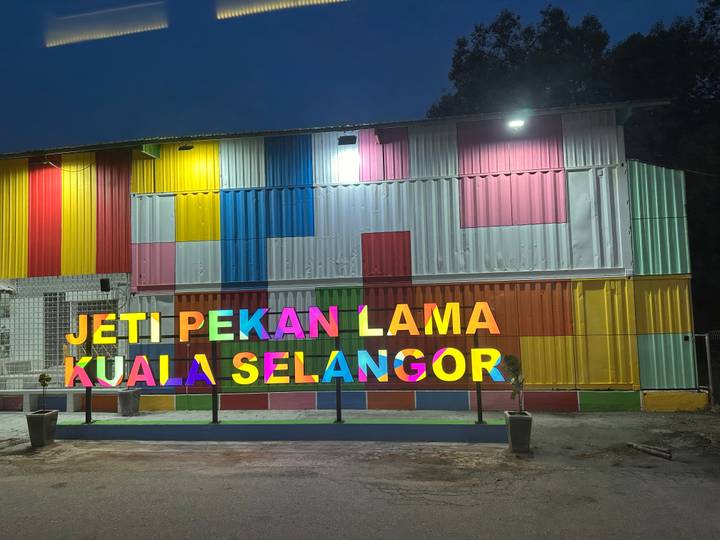 Colorful shipping-container building lit at night with sign reading 'Jeti Pekan Lama Kuala Selangor'.