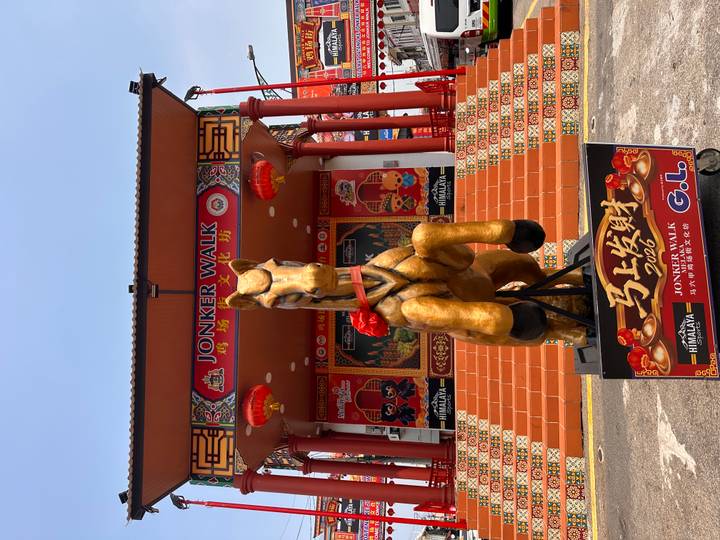 Golden horse statue with red bow in front of ornate Jonker Walk stage in Melaka.