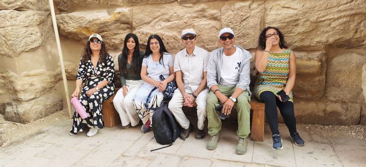 Small tour group resting on wooden benches against a sandstone wall inside an ancient Egyptian site.