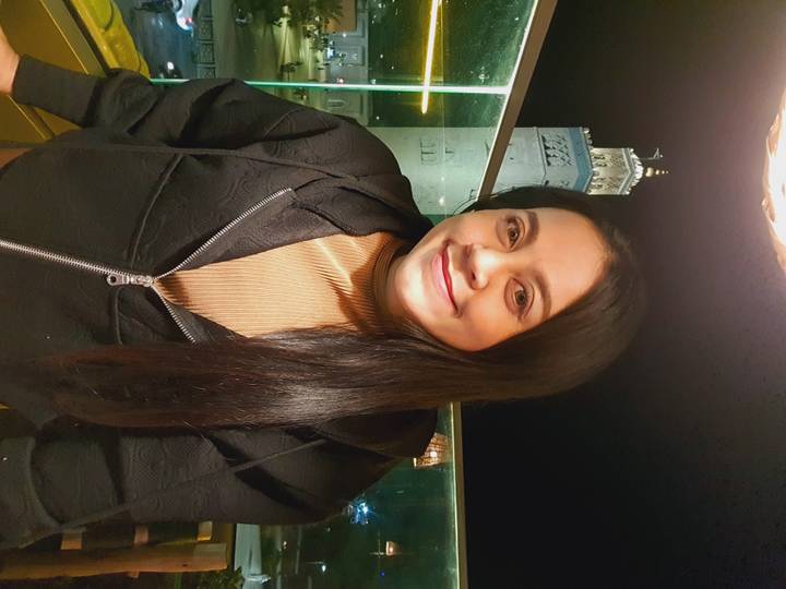 Night-time portrait of a woman with an illuminated mosque minaret in the background.