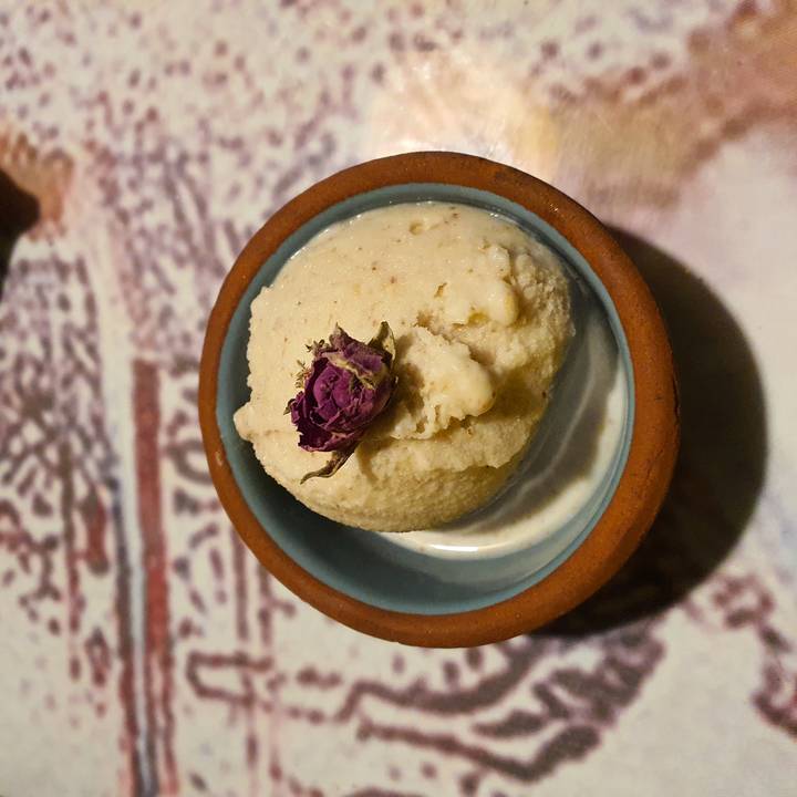 Close-up of a scoop of creamy dessert garnished with a dried rosebud in a ceramic bowl.