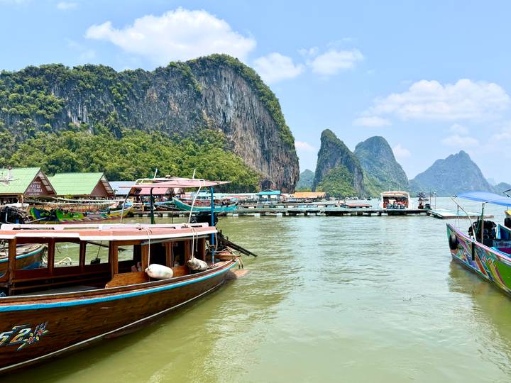 Floating village and long-tail boats moored against towering limestone cliffs in a green bay.