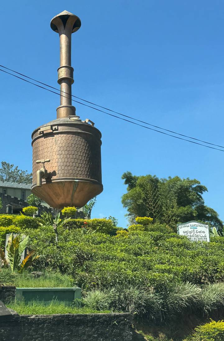 Large bronze tea pot monument standing in a roundabout against a clear blue Sri Lankan sky.