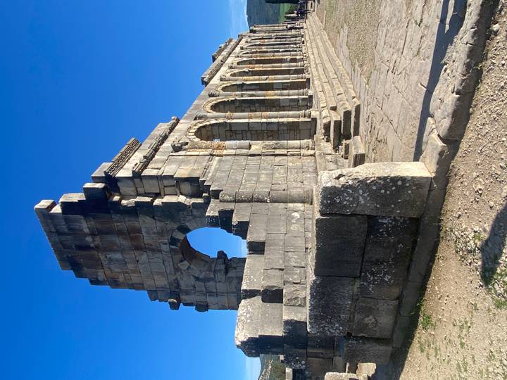 Well-preserved Roman arch and colonnade of Volubilis rising against a clear blue sky.