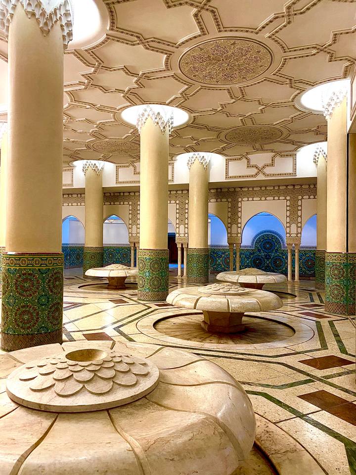 Elegant ablution hall with columns, ornate green tiles and stone fountains inside a Moroccan mosque.