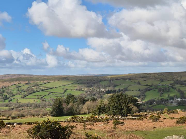 Expansive view of rolling green moorland and patchwork fields beneath a partly cloudy sky.