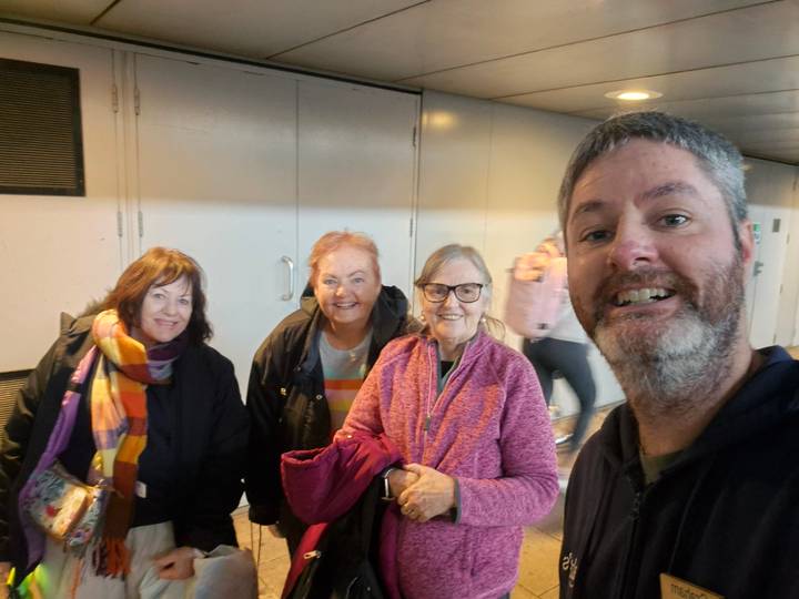 Smiling group selfie of four travellers inside a terminal corridor.