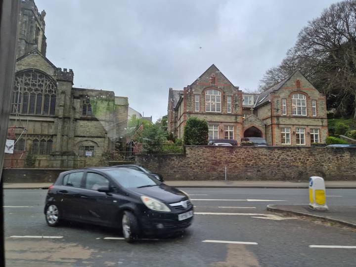 Blurred black car passing a stone church and historic building seen through a vehicle window.