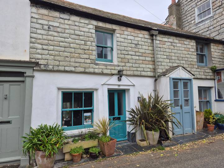 Charming white-washed cottage with teal doors and windows adorned by potted plants.