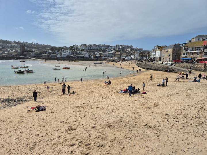 Busy sandy beach and shallow harbour waters at St Ives with families enjoying the spring sunshine.