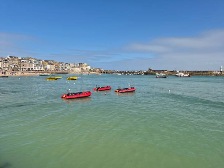 Clear turquoise harbour with red inflatable boats floating near the quays of St Ives.