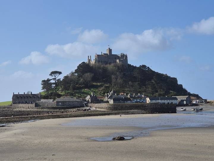 Medieval castle atop St Michael’s Mount rising above a small Cornish village at low tide.