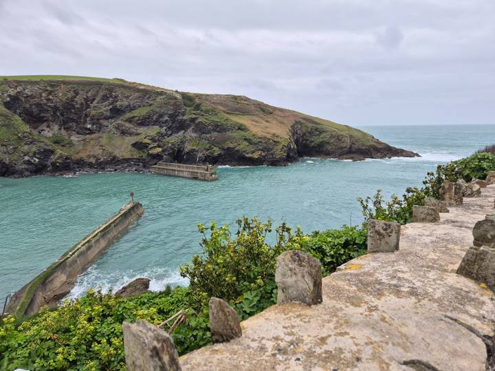 Turquoise inlet and rugged cliffs surrounding Boscastle harbour on a grey day.
