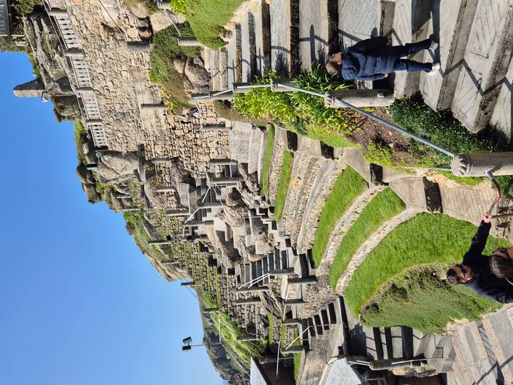 Stone terraces and steps of the open-air Minack Theatre carved into a cliffside with visitors exploring.