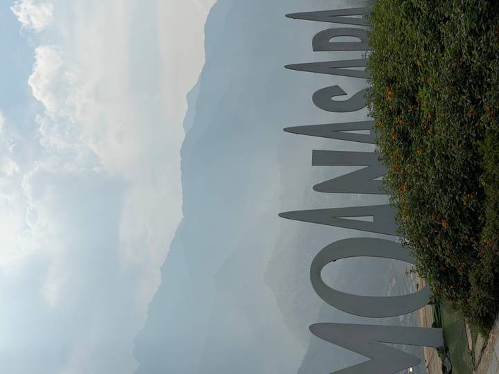 Misty mountain backdrop behind large sculptural letters in a landscaped garden.