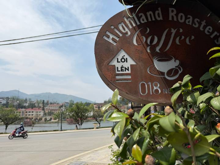 Close-up of a rustic coffee sign with a lake and mountains in the background.