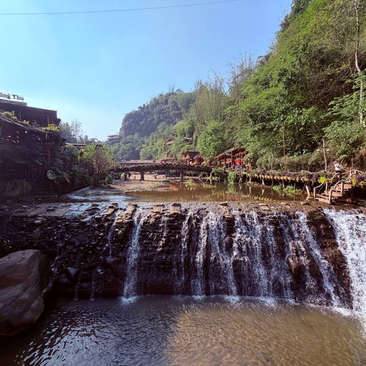 Scenic waterfall cascading over rocks with wooden bridges and lush greenery at Cat Cat.
