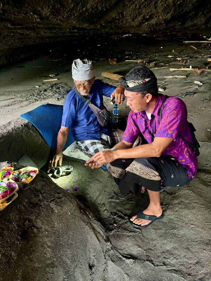 Local men preparing offerings in volcanic sand during a traditional Balinese ceremony at dusk.