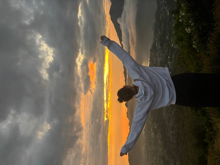 A woman with outstretched arms faces a dramatic sunrise over misty mountains and a valley blanketed with clouds.