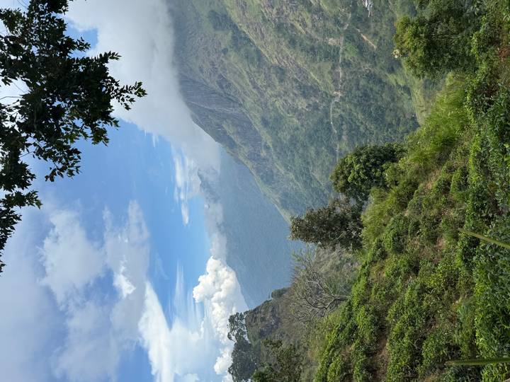 Lush green mountain valley with distant misty peaks beneath a blue sky and clouds.