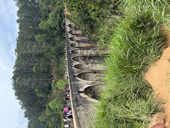 Historic Nine-Arch railway bridge spanning a lush ravine with tourists walking along the top.