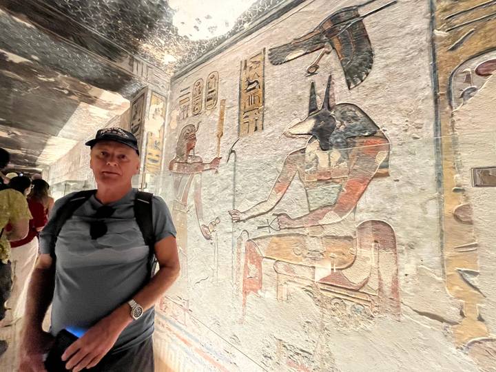 Visitor stands beside vividly painted reliefs of Egyptian gods inside a tomb