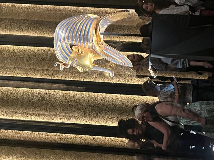 Golden funerary mask displayed in a museum with visitors gathered around