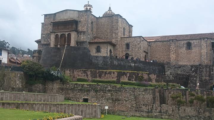 Stone Inca-Spanish church complex with dark retaining walls and bell tower under cloudy sky.