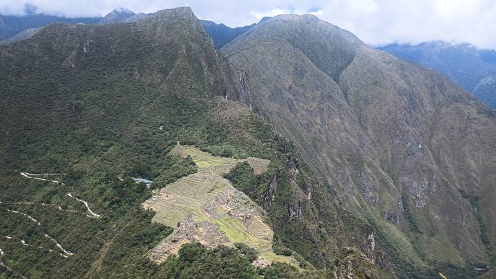High viewpoint over steep forested mountains with terraced ruins visible on a ridge.