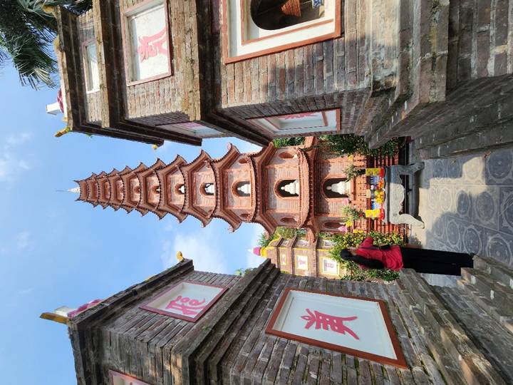 Tall red brick pagoda rising above ornate shrines and offerings under a bright blue sky.