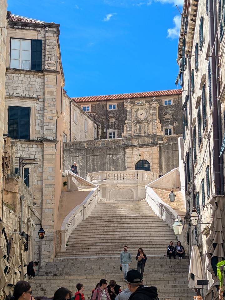 Historic stone staircase and clock tower in a sunlit Mediterranean old town.