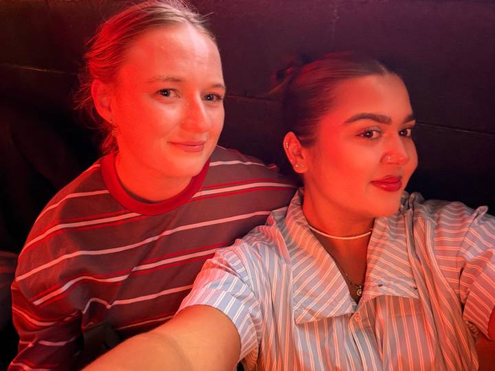 Two women enjoying nightlife under red ambient lighting, smiling for a selfie.