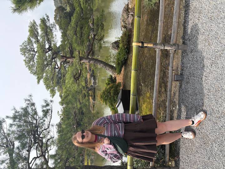 Traveler posing beside a manicured pond and sculpted pine trees in a Japanese garden.