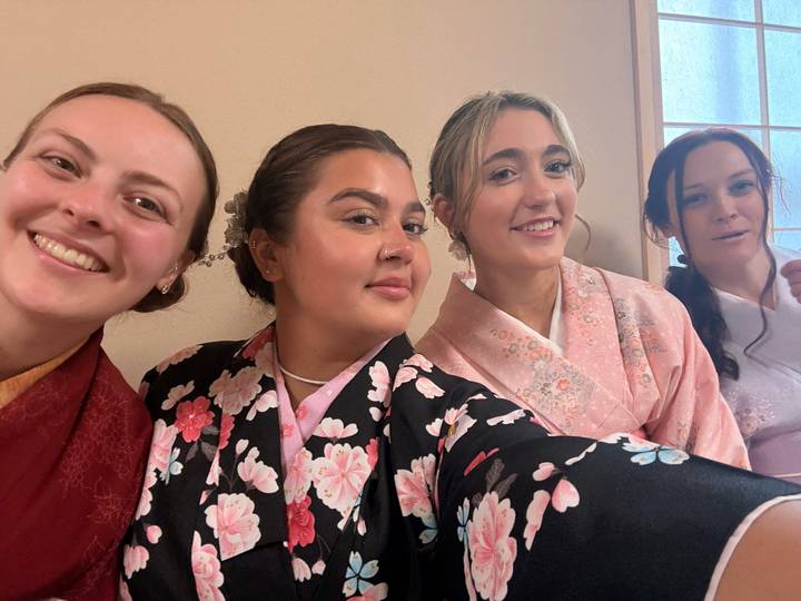 Four young women in colorful kimonos smiling for a close-up selfie indoors.