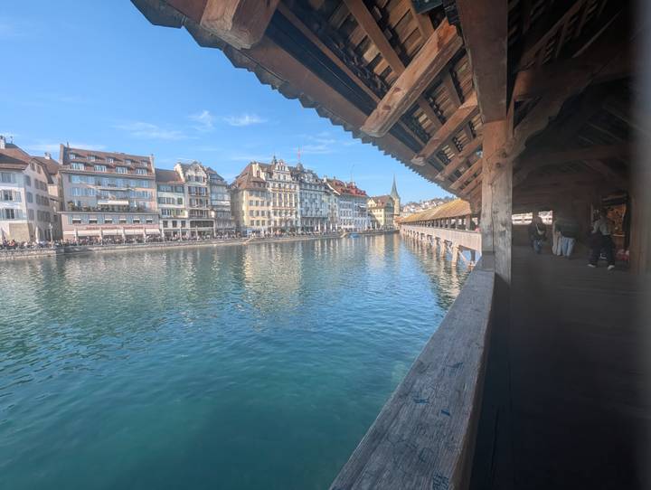 View along Lucerne's wooden Chapel Bridge over turquoise lake water and historic waterfront buildings.