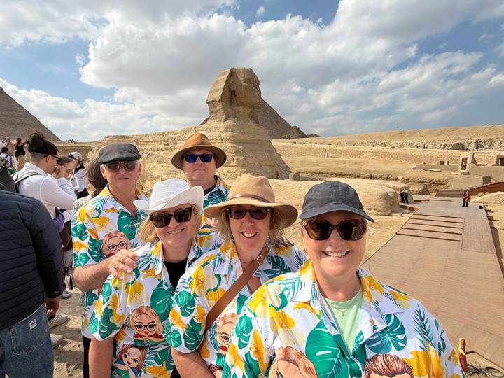 Group smiling before the Sphinx with desert sands and pyramids in the background.