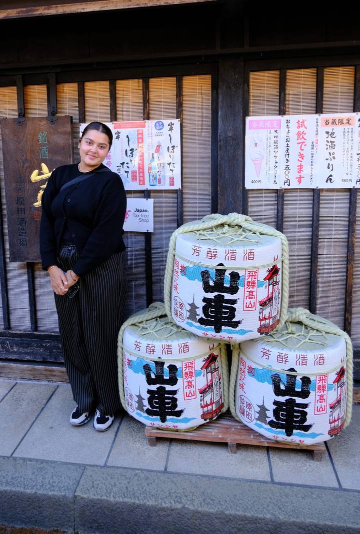 Traveller poses beside decorative sake barrels outside a traditional Japanese shop