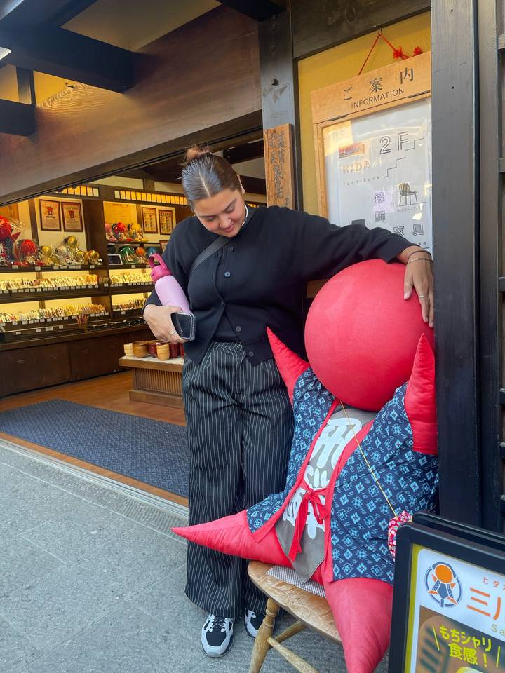 Visitor smiles while hugging a large red Sarubobo doll outside a souvenir shop