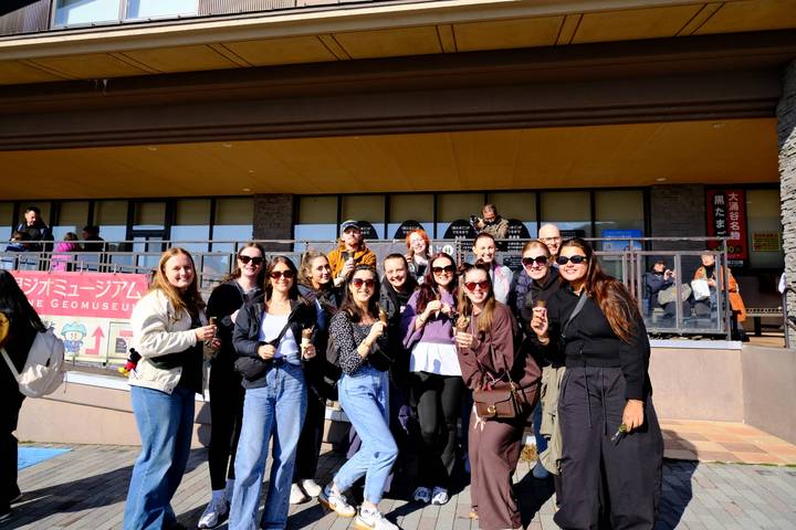 Smiling tour group poses outside a Japanese museum building on a sunny day