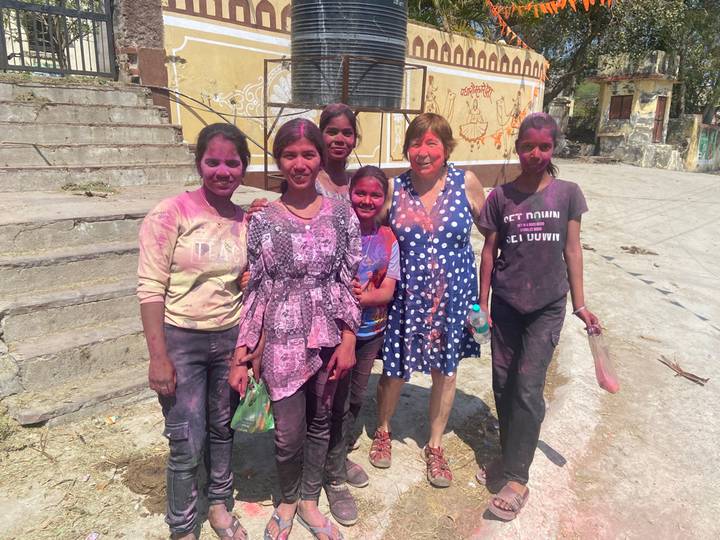 Women joyfully covered in vibrant Holi powders pose together in an Indian village street