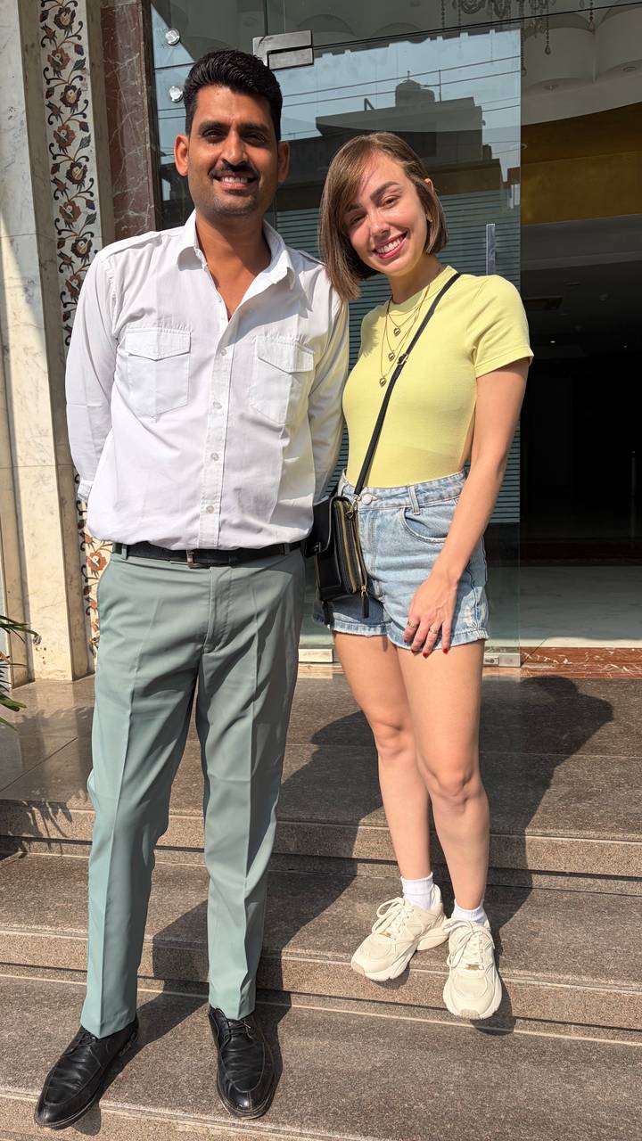 Guide and traveller pose outside a storefront on a sunny day