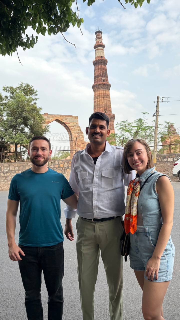 Two tourists stand with their Indian guide in front of historic sandstone arches