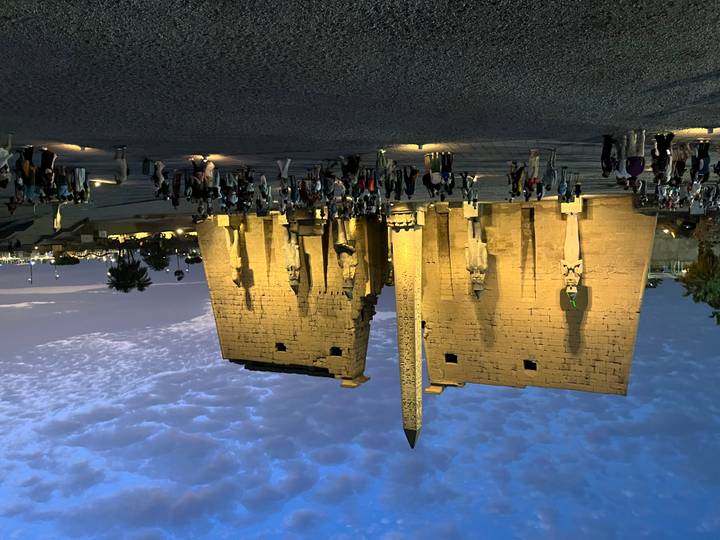 Luxor Temple illuminated at blue hour with an obelisk and colossal statues, crowds standing in the forecourt.