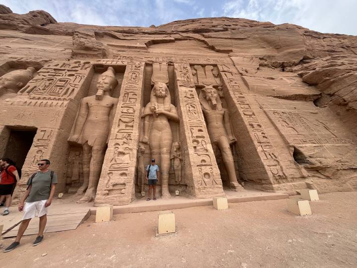 Rock-cut façade of Abu Simbel’s smaller temple with hieroglyphics; a tourist stands between carved figures.