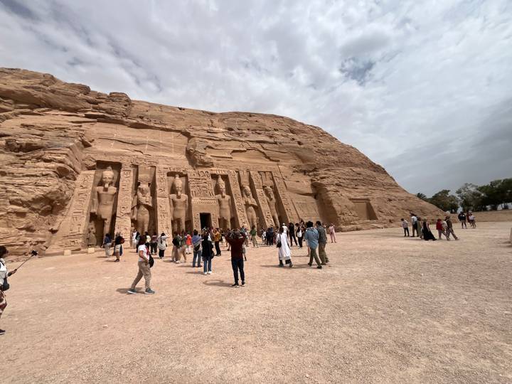 Wide shot of Abu Simbel’s façade carved into sandstone cliff, with numerous visitors scattered across the forecourt.