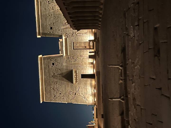 An ancient Egyptian temple illuminated at night, reliefs visible on the facade.