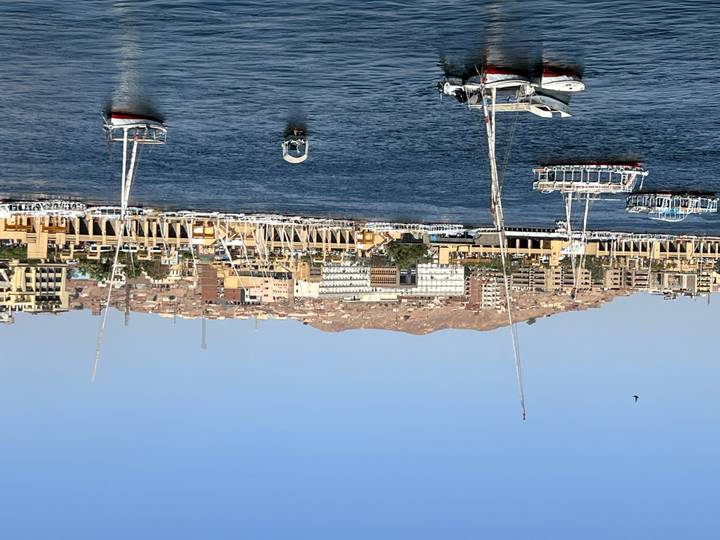 Daytime view over the Nile with sailboats moored opposite a hillside cityscape in Aswan.